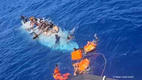 A picture taken by the Italian coast guard shows one of the upturned boats, with some migrants clinging to it, while others make their way towards the rescuers with the help of buoyancy aids | Photo: Italian Coast Guard Guardia Costiera