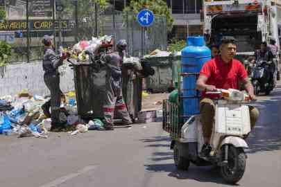 Syrian waste workers collect garbage as a Syrian delivery man transports gas bottles in Beirut, Lebanon, May 3, 2023.