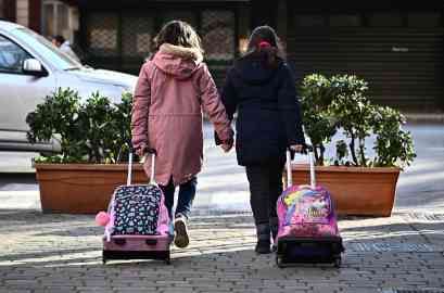 Two little girls holding hands as they go to school dragging their backpacks. | Photo: ARCHIVE/ANSA/LUCA ZENNARO