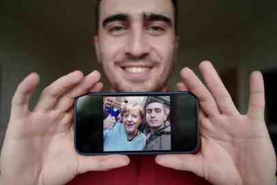 Syrian refugee Anas Modamani posing in his flat in Berlin on September 1, 2021, displaying the selfie he took with German Chancellor Angela Merkel outside a refugee center in Berlin on September 10, 2015, when he was 18 years old | Photo: AFP/John MacDougall via ANSA