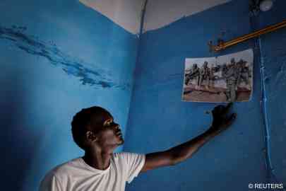 Fisherman Birane Mbaye, points at a group picture on his wall which shows his fishermen friends, three of whom have succeeded in their journey to reach Spain, one who died at sea and others who are still in Fass Boye, Senegal, March 19, 2024. | Photo: REUTERS/Zohra Bensemra 