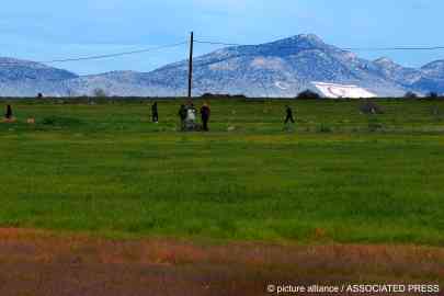 Migrants are seen walking near the Pournara migrant reception center in the Republic of Cyprus earlier this year - while in the distance, the flag of the self-declared TRNC is seen etched into the ground | Photo: Picture-alliance