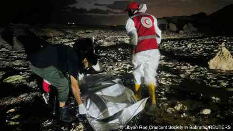A member of the Red Crescent walks next to a body bag in a location given as near Surman, Libya, after a migrant boat capsized west of Libya's capital Tripoli | Photo: Libyan Red Crescent Society in Sabratha/ Reuters
