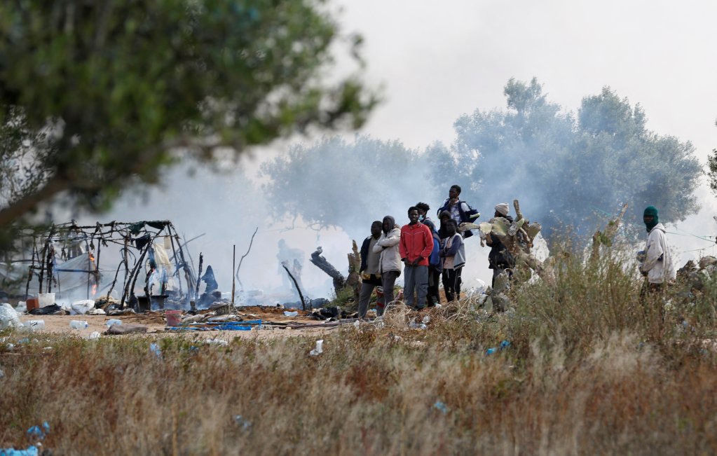Des migrants se tiennent près d'un abri de fortune incendié lors du démantèlement de leur campement, le 24 avril 2025, à El-Amra, près de Sfax, en Tunisie. Crédit : Reuters