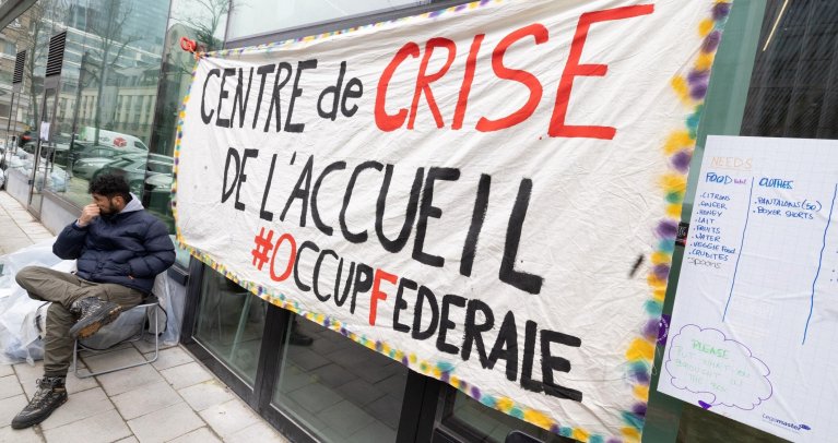 Un homme est assis à côté d'une banderole indiquant "centre d'accueil de crise" devant le bâtiment du futur Centre national de crise, occupé par des demandeurs d'asile à Bruxelles, le 20 mars 2023.