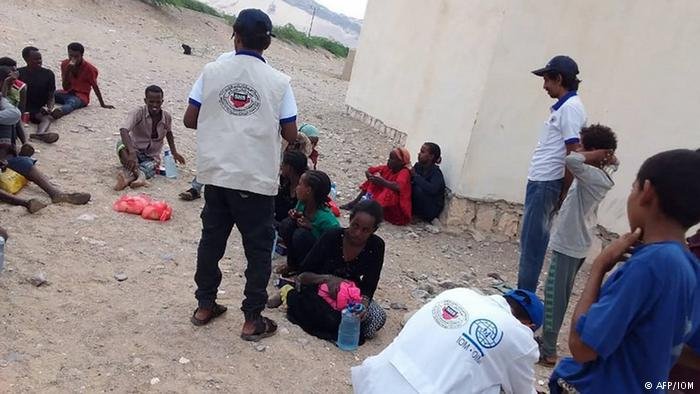 Aid workers stand with migrants after their boat capsized off the shore of Yemen (AFP/IOM)